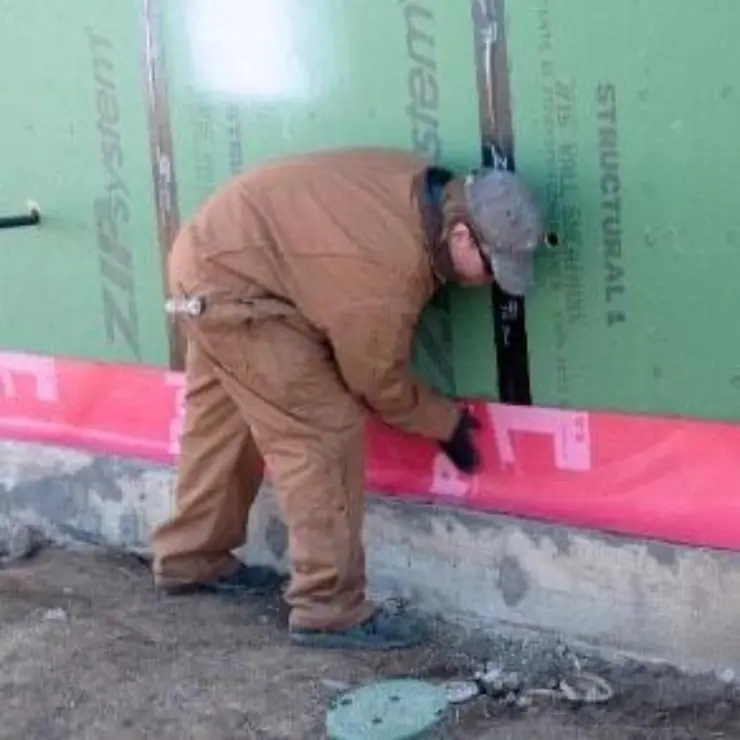 A worker installs a termite barrier around the foundation of a building.