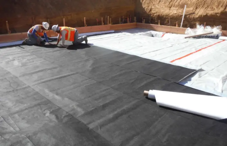 Construction workers installing waterproofing membrane on a building foundation.